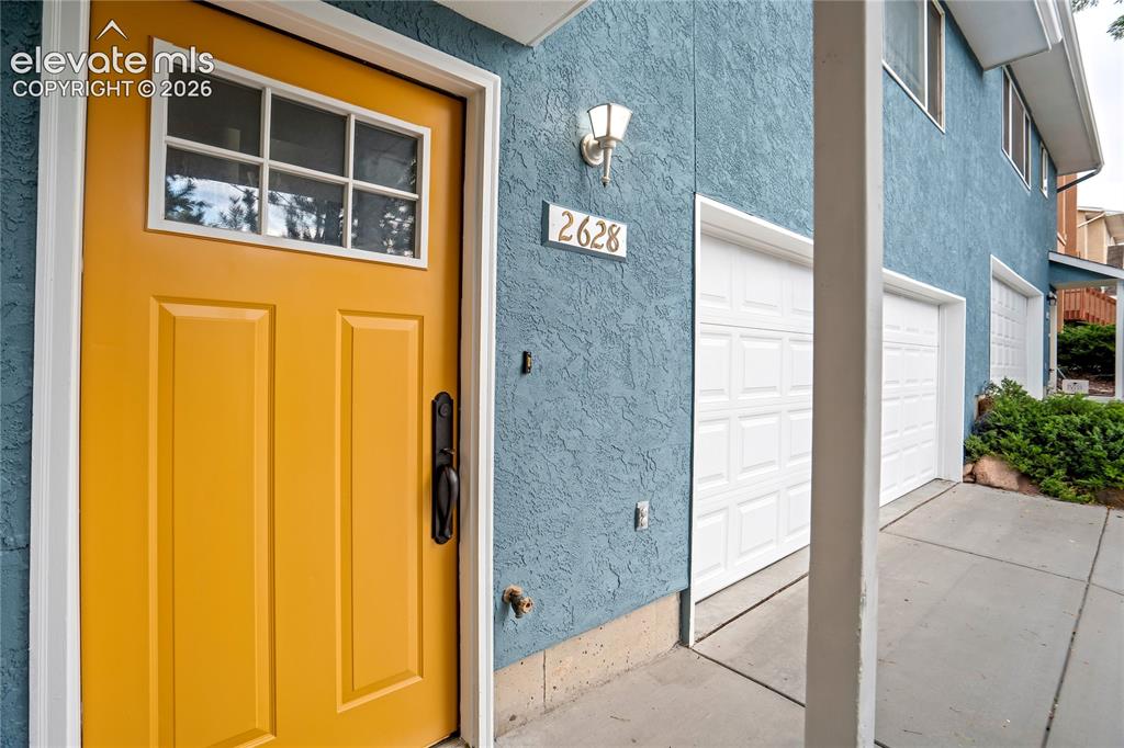 Image 2 of 50: Vibrant entry door with decorative glass panels and dark hardware, stucco e
