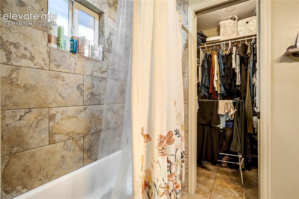 Image 23 of 50: Bathtub with a tiled surround, recessed window, and a built-in shelf