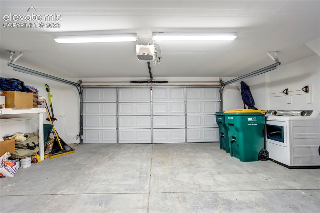 Image 26 of 50: Garage with a concrete floor, white panel garage door, and overhead lightin