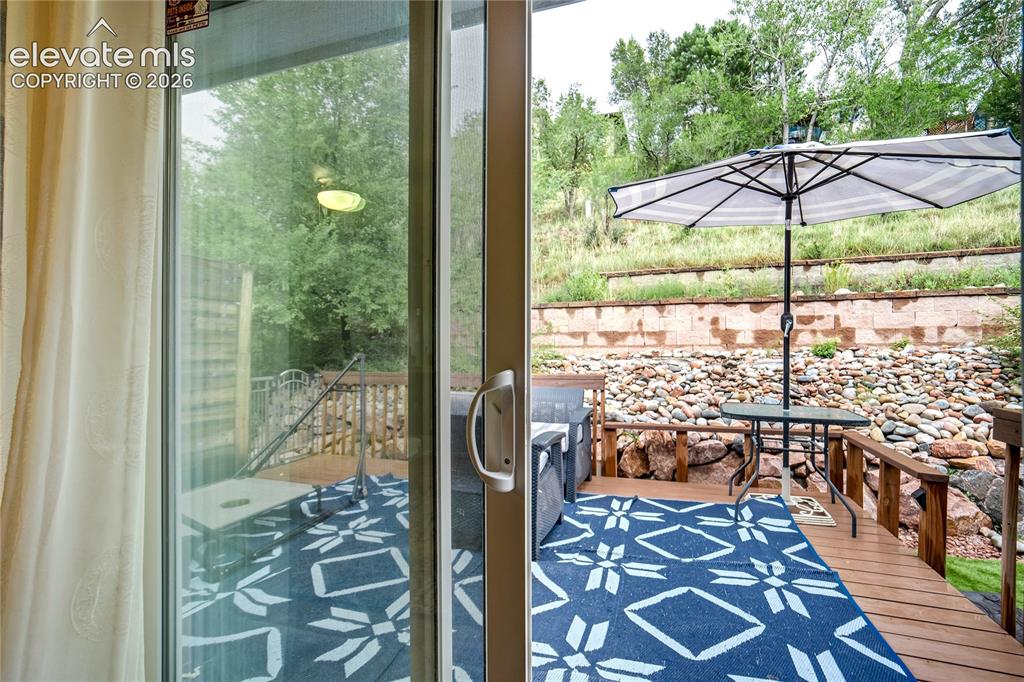 Image 27 of 50: Sliding glass door leading to an outdoor deck with wood railings, a stone r