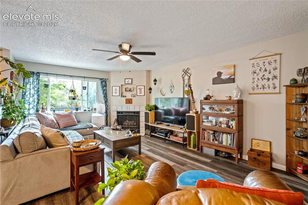 Image 29 of 50: Living area featuring wood-finish flooring, a ceiling fan, and a fireplace 