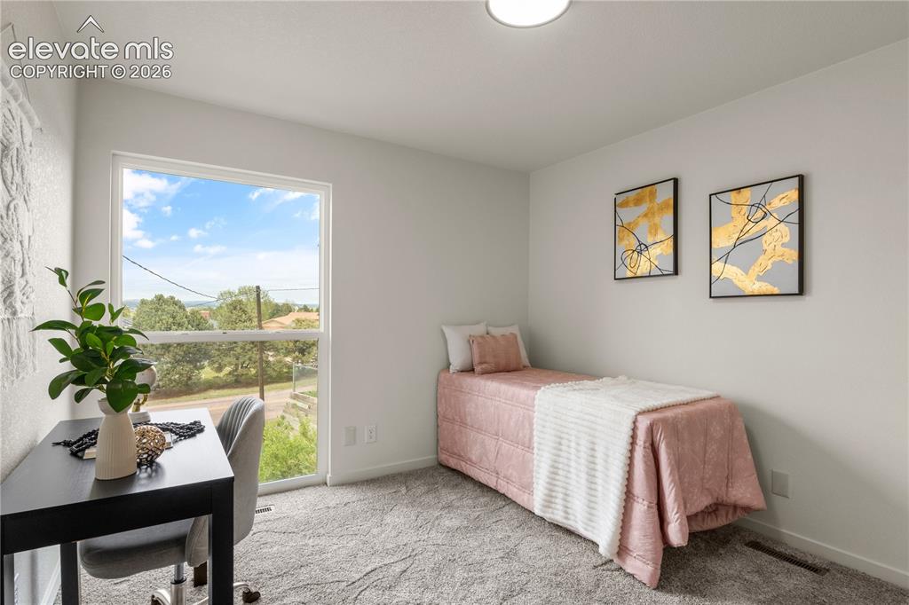 Image 15 of 30: Bright room featuring a large window, soft gray carpeting, white walls, and