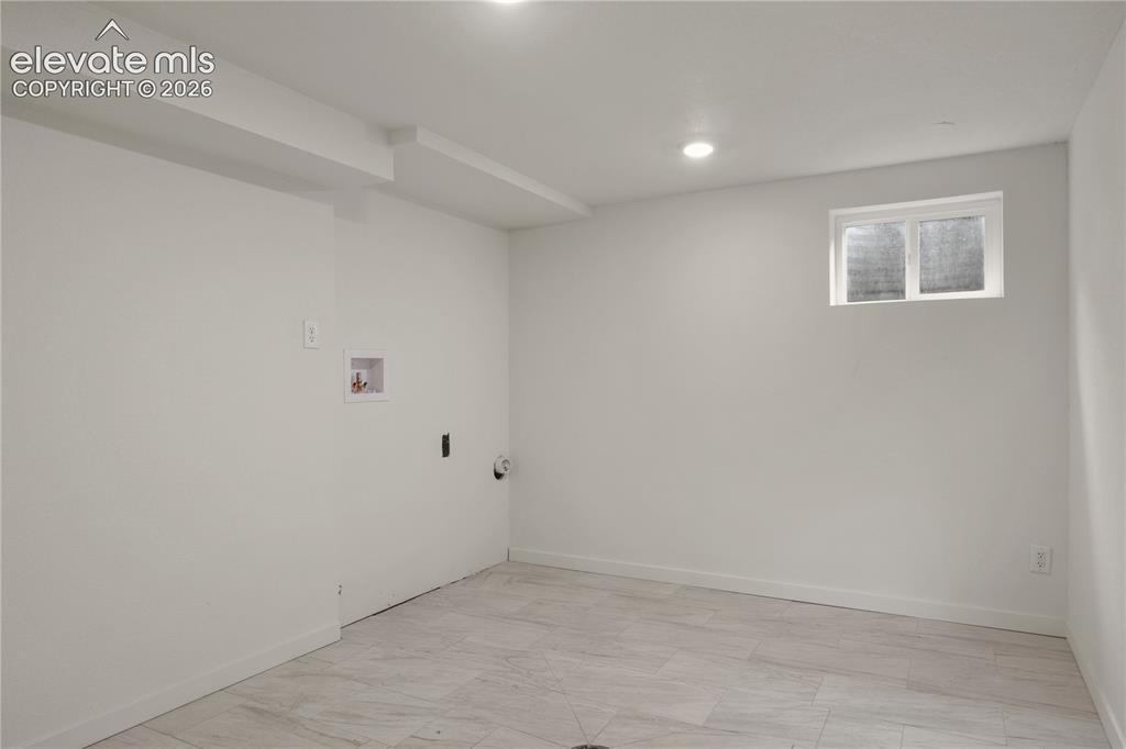 Image 27 of 30: Bright lower-level room featuring light-colored walls and wood-finish tile 