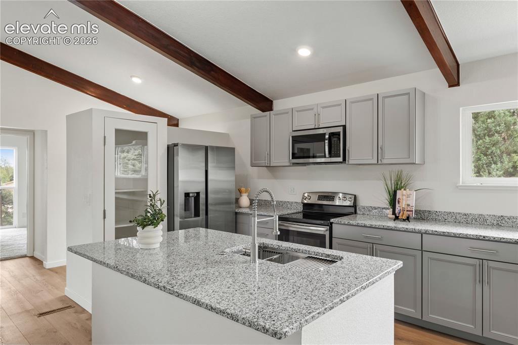 Image 9 of 30: Kitchen featuring an island with an undermount sink, light gray cabinetry, 