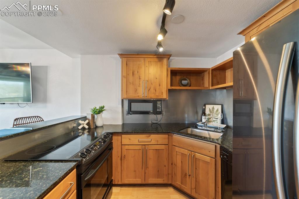 Image 8 of 32: Kitchen with black appliances, a sink, open shelves, and dark stone counter