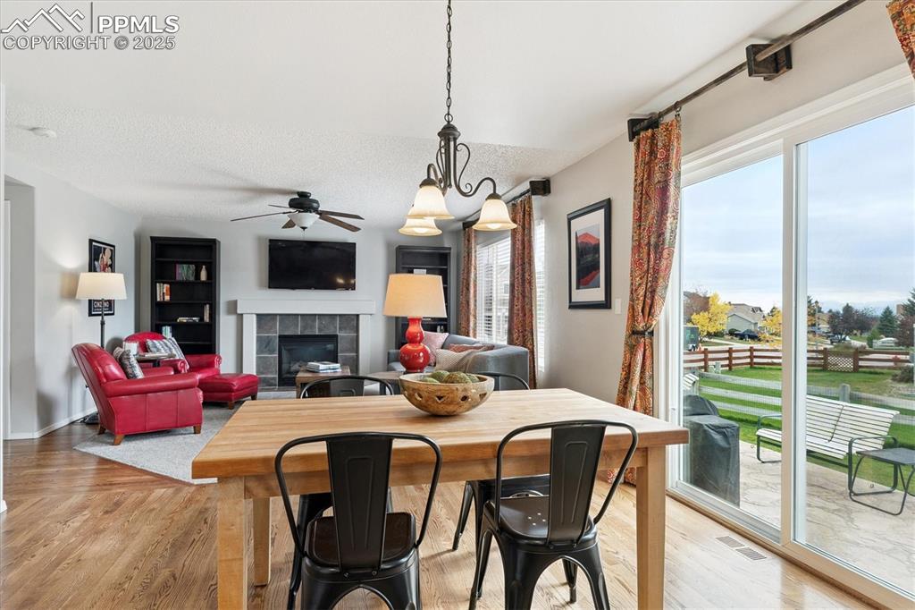 Image 15 of 40: Dining area with a tiled fireplace, light wood-style flooring, a ceiling fa
