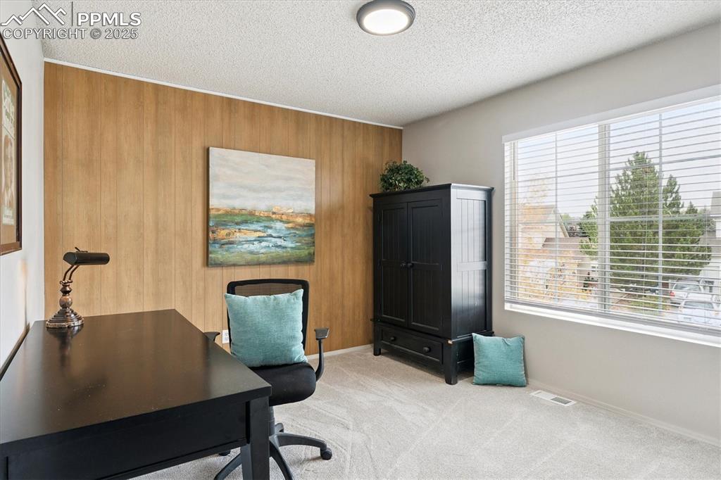 Image 21 of 40: Home office with light colored carpet, wood walls, and a textured ceiling