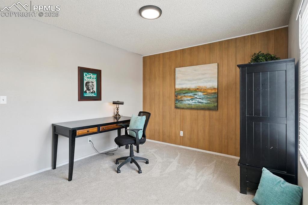 Image 22 of 40: Carpeted office with wooden walls and a textured ceiling