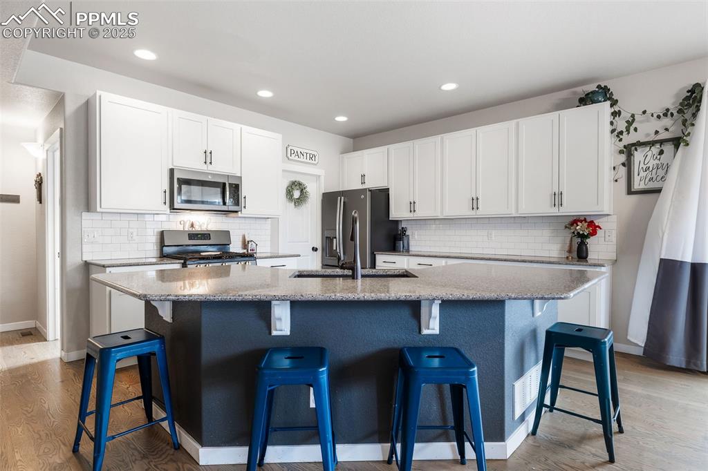 Image 11 of 43: Kitchen featuring white cabinetry, a kitchen bar, a kitchen island with sin