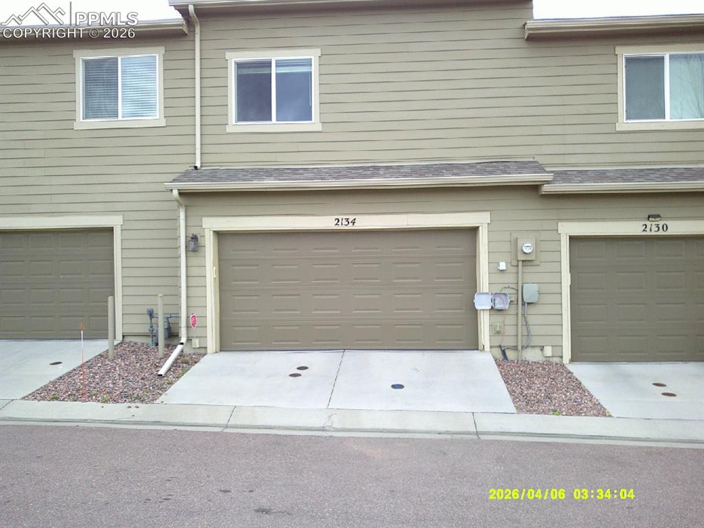 Image 12 of 13: The property features light tan siding, two windows, and an integrated gara