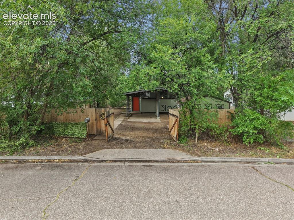 Image 36 of 36: Gated entry with a wooden fence, asphalt driveway, and mature landscaping