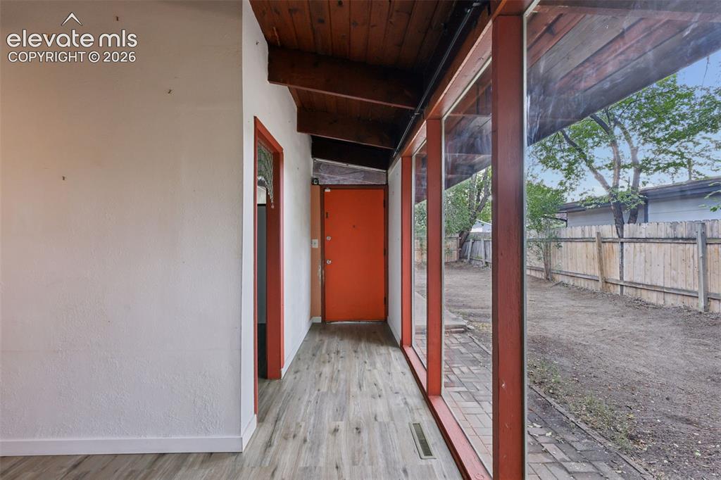 Image 8 of 36: Wood-finish flooring with a vibrant orange entry door, exposed wood ceiling