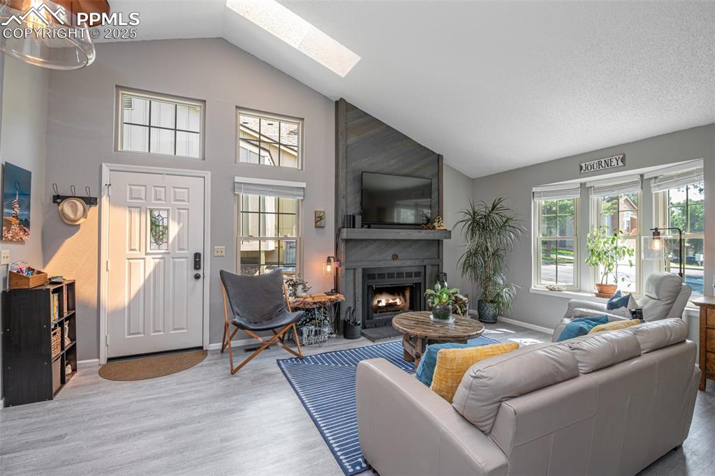 Image 7 of 27: Living room featuring skylights, a large fireplace, and high vaulted ceilin