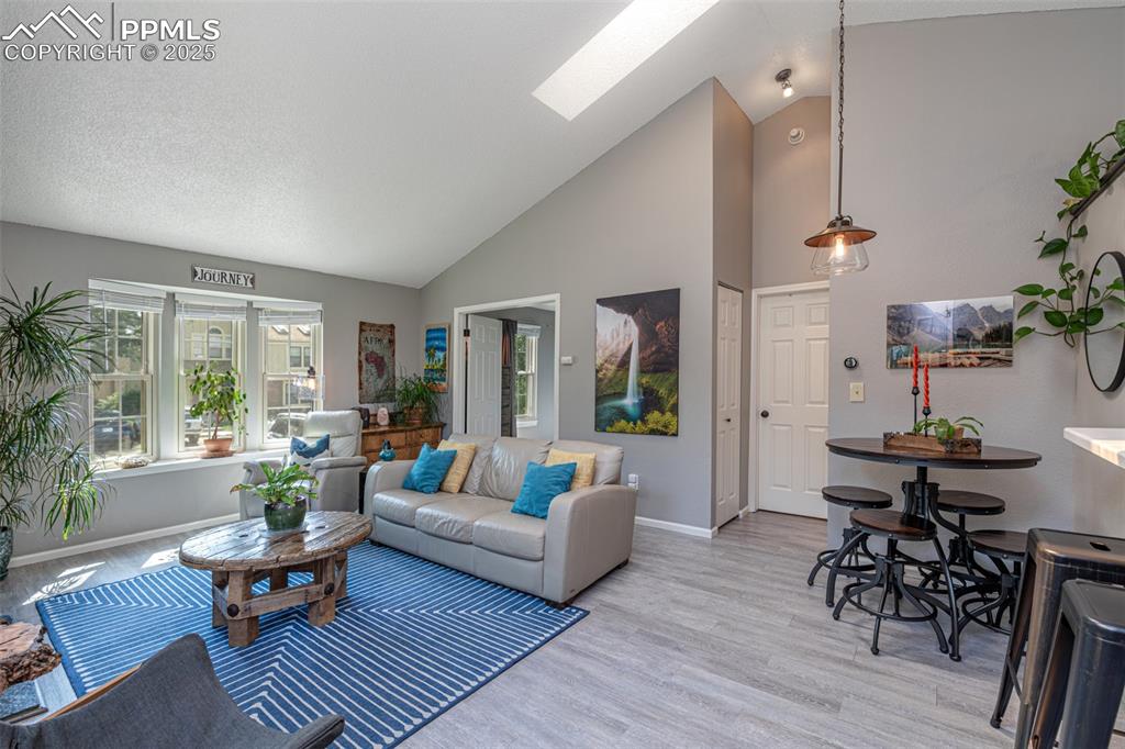 Image 8 of 27: Living room featuring light wood-style flooring, high vaulted ceiling, skyl