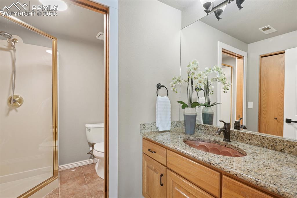 Image 29 of 37: Bathroom with tile patterned flooring, vanity, toilet, and an enclosed show