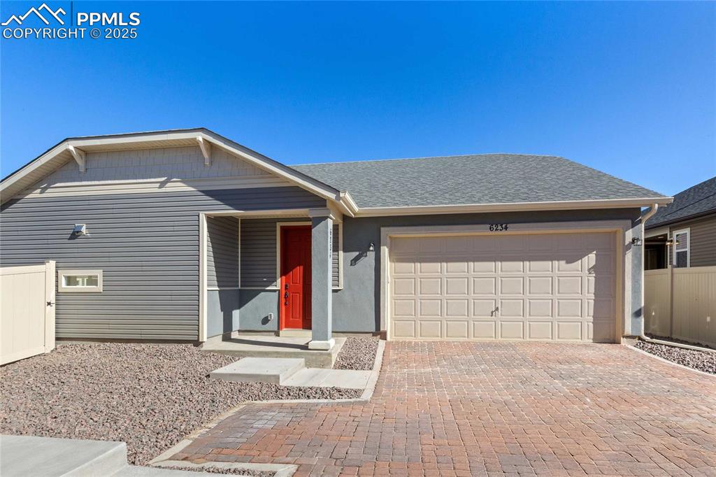 Caption: Ranch-style house with a shingled roof, decorative driveway, an attached garage, and stucco siding
