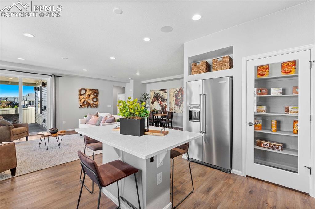 Image 11 of 27: Kitchen with high end fridge, a kitchen bar, light stone counters, recessed