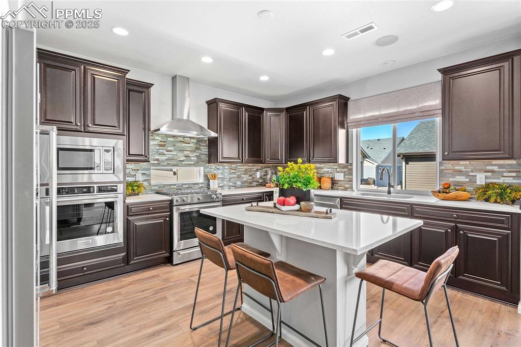 Image 12 of 27: Kitchen with a breakfast bar area, light stone counters, dark brown cabinet