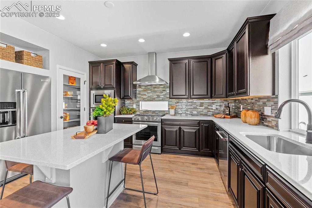Image 13 of 27: Kitchen featuring a breakfast bar area, light stone countertops, dark brown