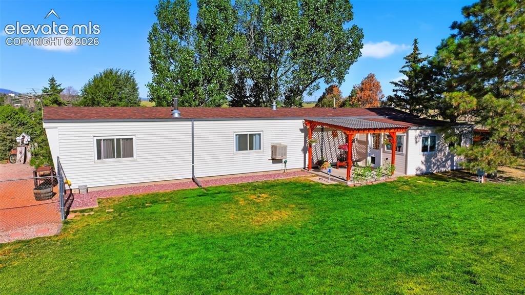 Image 16 of 50: Expansive lawn area with a covered patio featuring a corrugated roof and wo