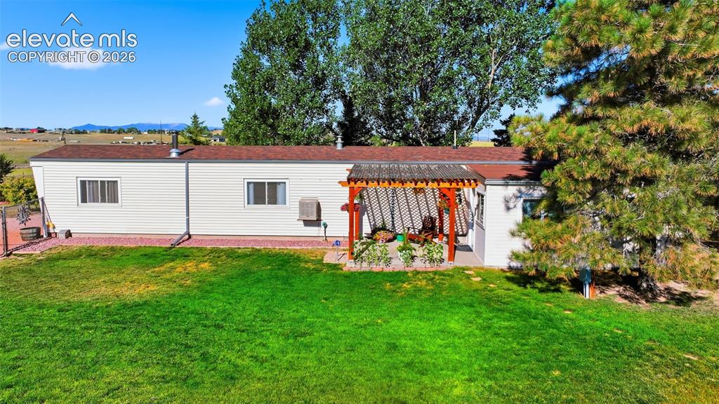 Image 17 of 50: White siding exterior with a red roof, featuring a wooden pergola over a pa