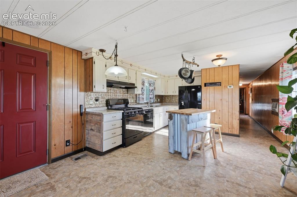 Image 23 of 50: Kitchen featuring wood paneling, white cabinetry, a black range, and a corr