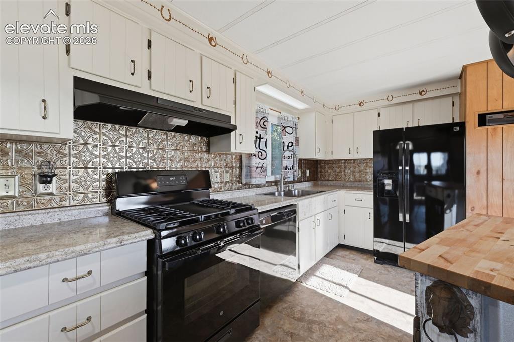 Image 25 of 50: White cabinetry, patterned backsplash, black range, black refrigerator, and