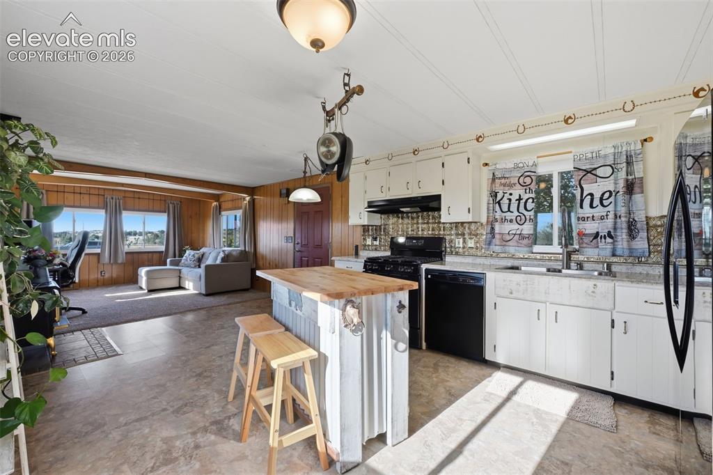 Image 26 of 50: Kitchen featuring white cabinetry, black appliances, a butcher block island