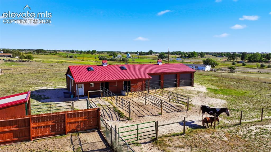 Image 3 of 50: Barn structure with a red metal roof, multiple stalls, and an attached gara