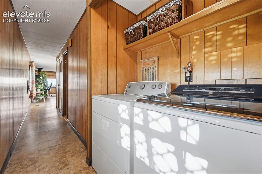 Image 31 of 50: Laundry area featuring wood-paneled walls and a built-in wood shelf