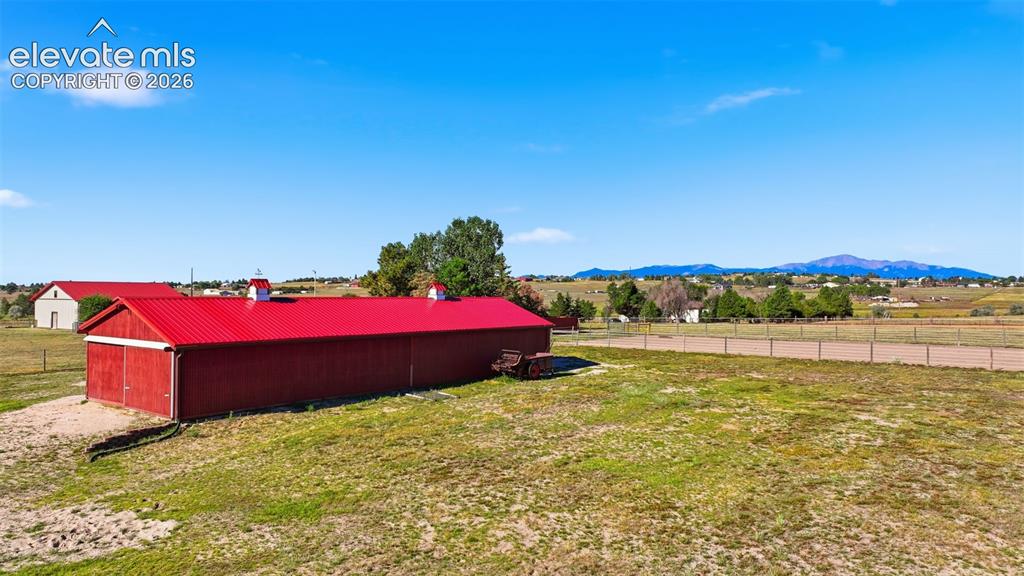 Image 38 of 50: Red barn structure with a metal roof, expansive open area, and distant moun