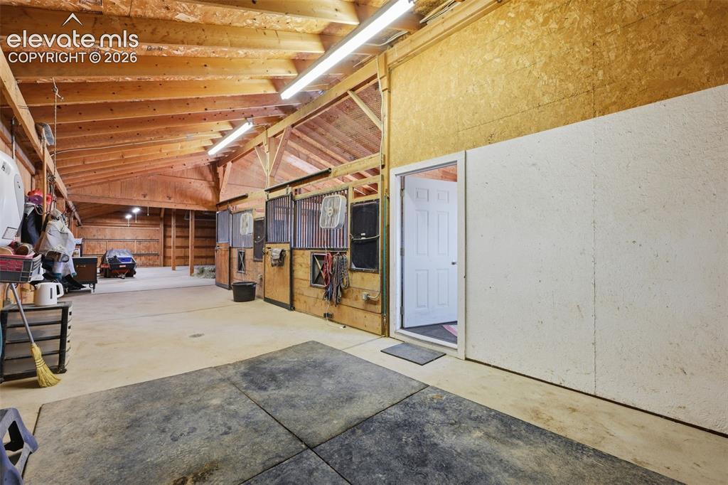 Image 40 of 50: Exposed wood-beam vaulted ceiling with fluorescent lighting, multiple stall