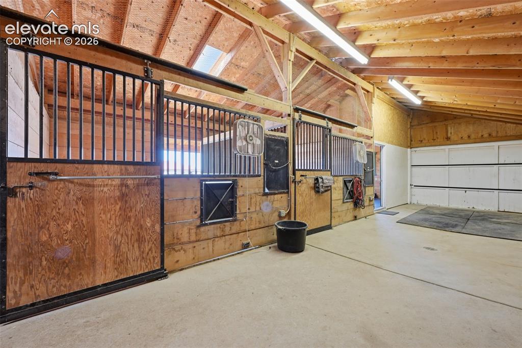 Image 41 of 50: Barn interior featuring multiple stalls with metal grates, exposed wood bea