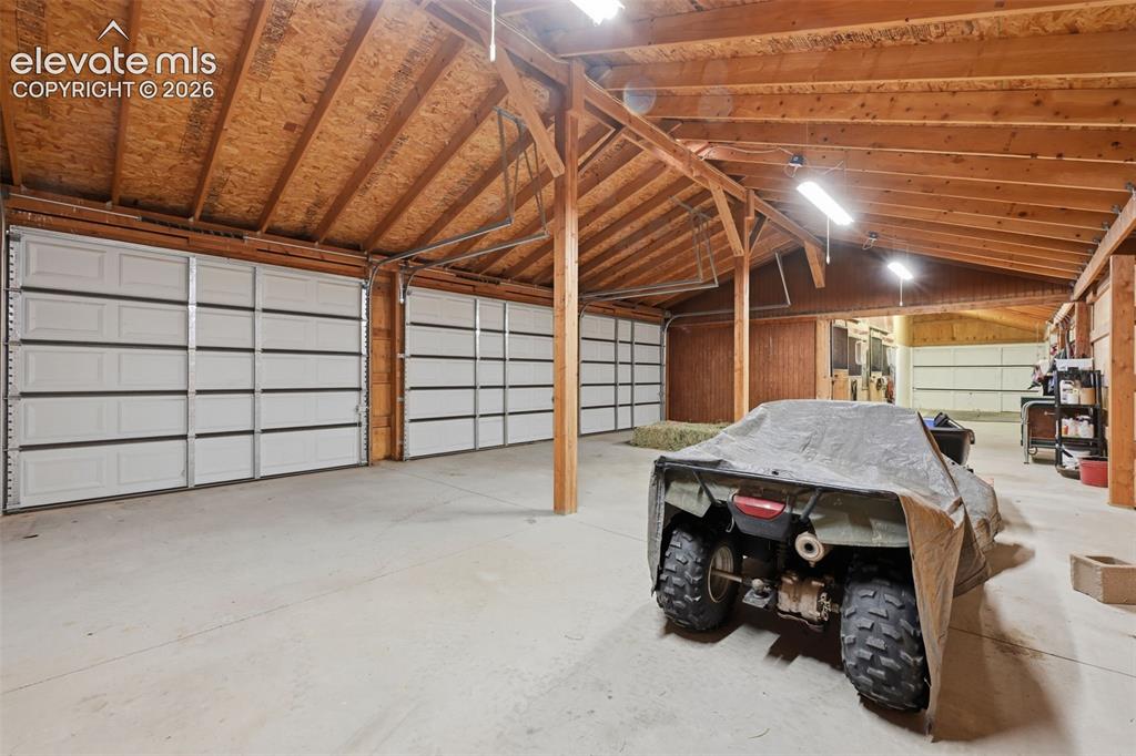 Image 44 of 50: Spacious multi-bay garage with concrete flooring, exposed wood beam ceiling