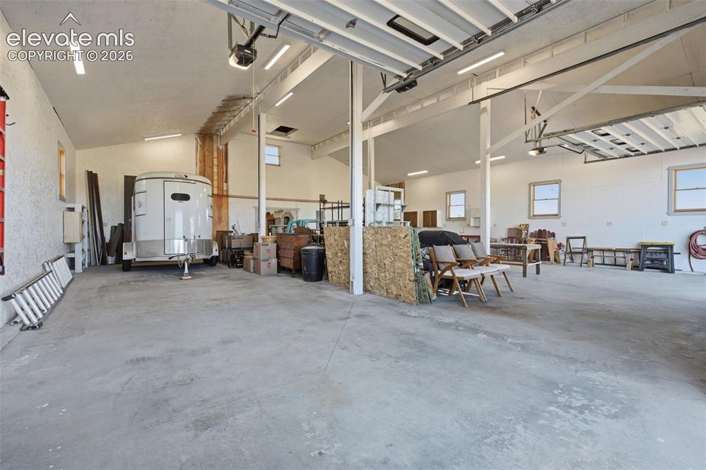 Image 47 of 50: Spacious concrete-floored garage with multiple windows, exposed beam ceilin