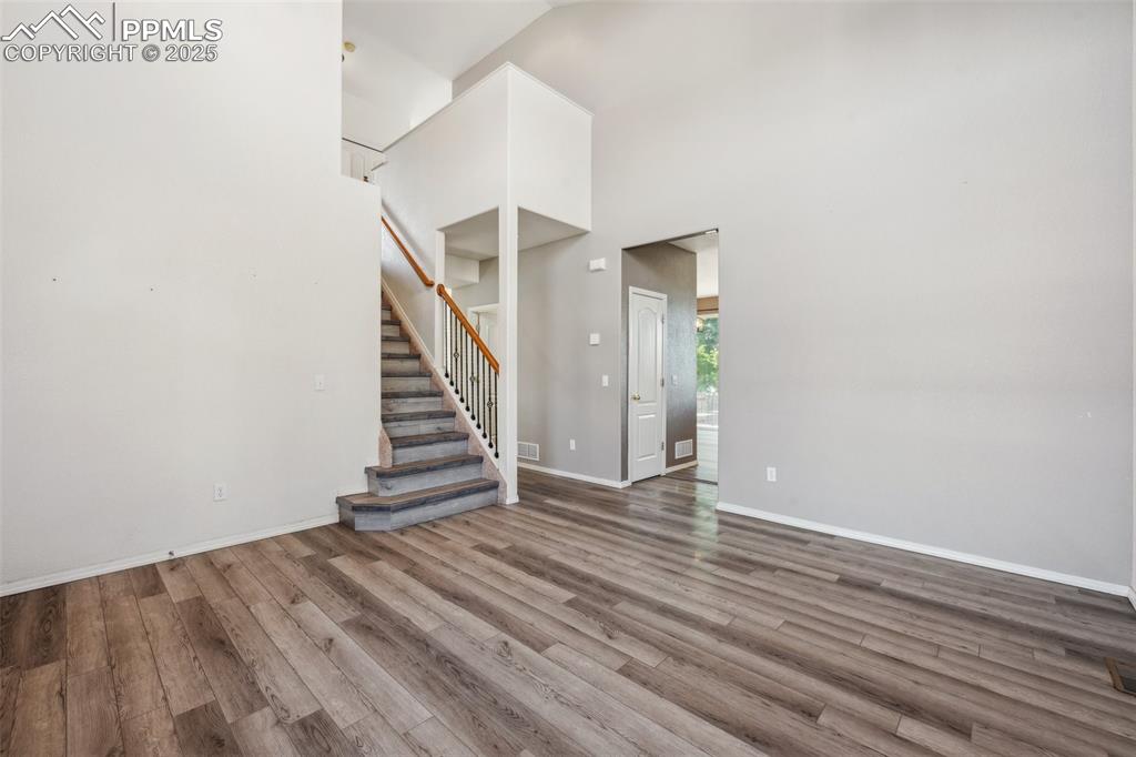 Image 10 of 38: Unfurnished living room with wood finished floors, stairs, and a high ceili