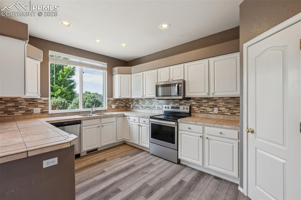 Image 12 of 38: Kitchen with appliances with stainless steel finishes, white cabinetry, lig