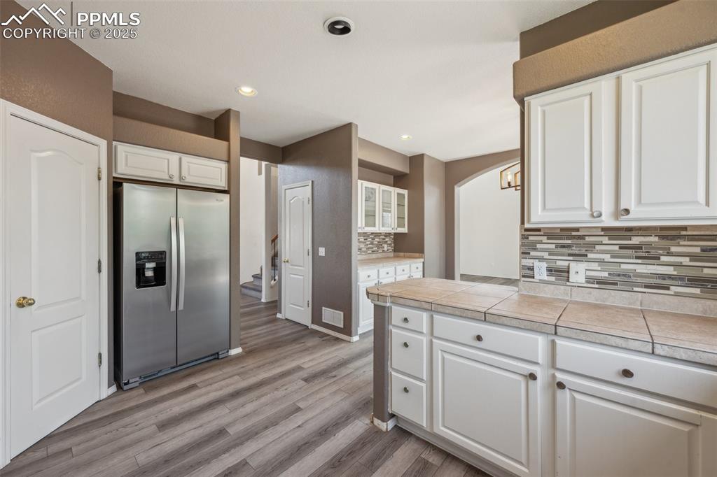 Image 14 of 38: Kitchen with stainless steel fridge, white cabinetry, light wood-style floo