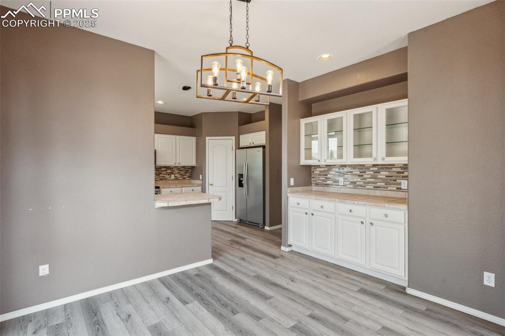 Image 18 of 38: Kitchen featuring a chandelier, decorative backsplash, light wood-style flo