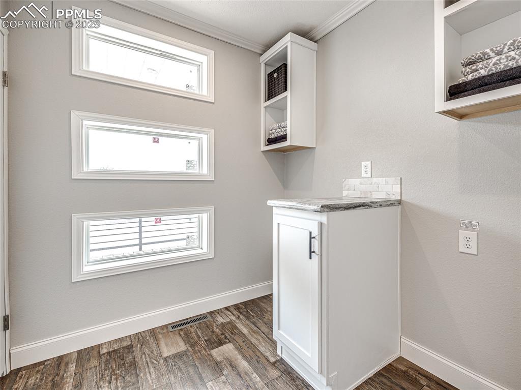 Image 12 of 25: Laundry area with crown molding and dark wood-style floors