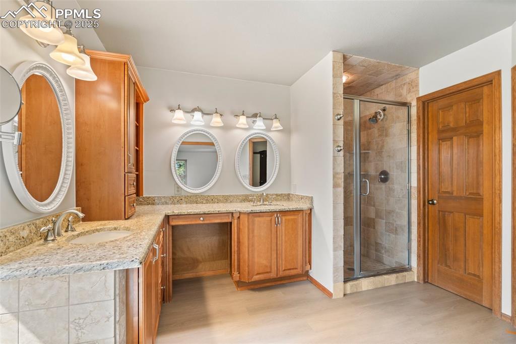 Image 16 of 26: Bathroom featuring wood finished floors, double vanity, and a shower stall