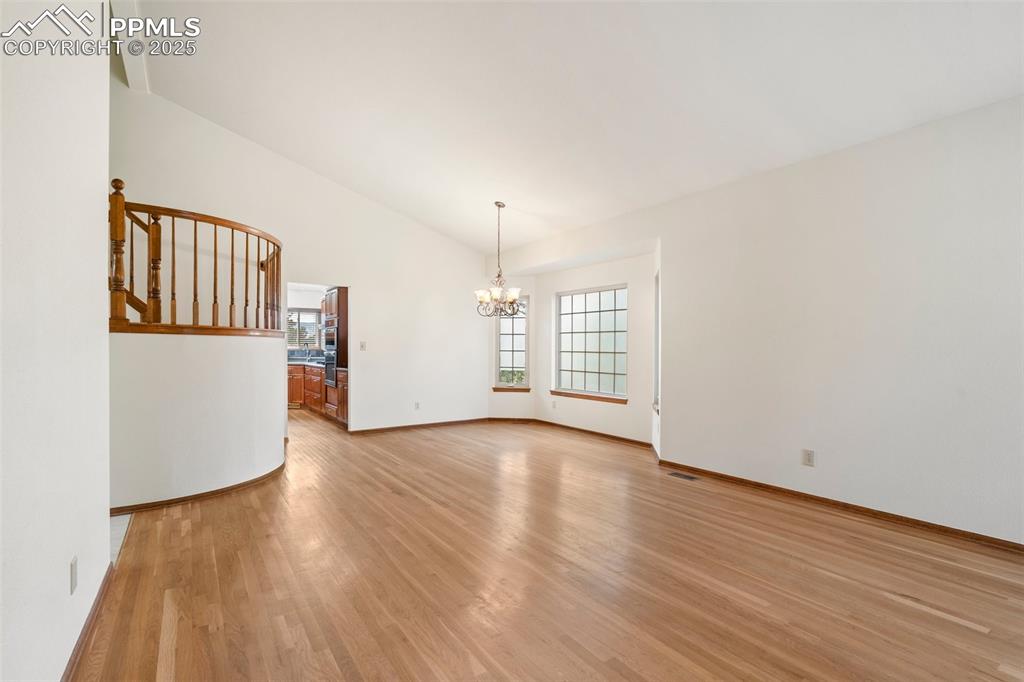 Image 3 of 26: Spare room featuring a chandelier, light wood-style floors, lofted ceiling,