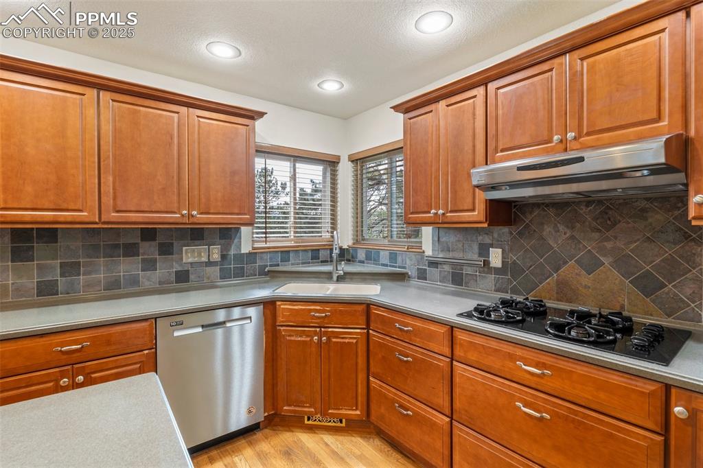 Image 7 of 26: Kitchen with dishwasher, black gas cooktop, under cabinet range hood, light