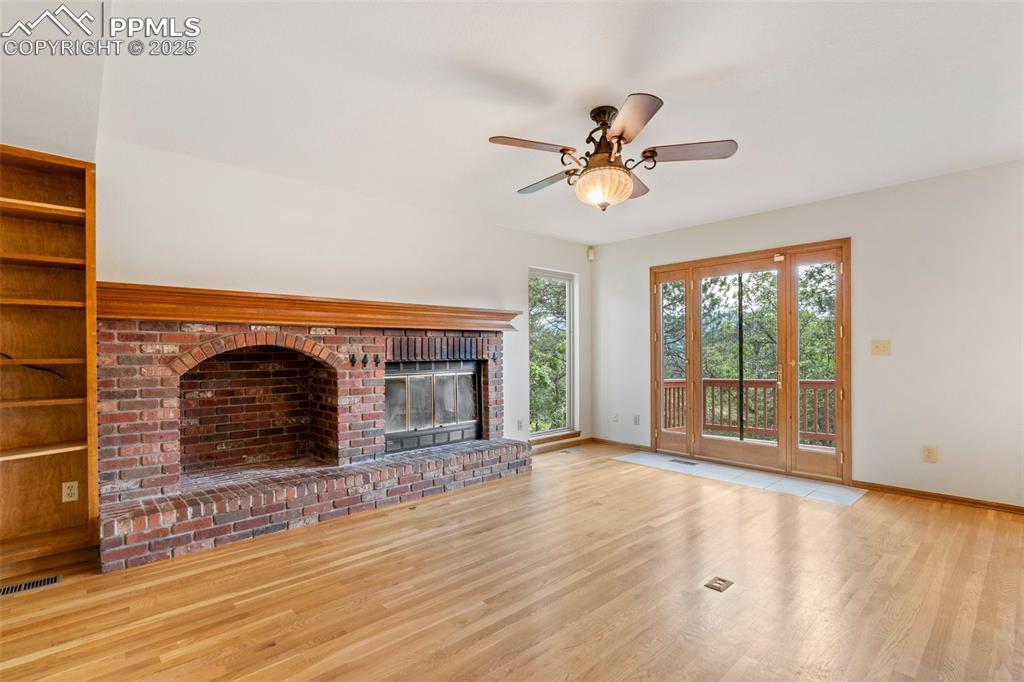 Image 9 of 26: Unfurnished living room with wood finished floors, ceiling fan, and a brick