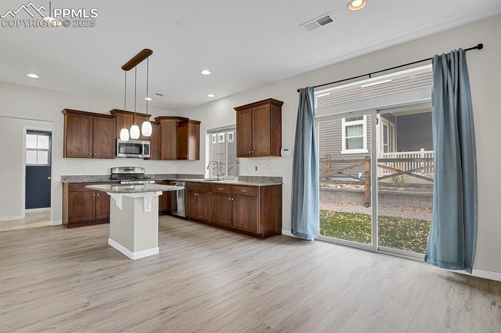 Image 8 of 30: Kitchen featuring pendant lighting, dark brown cabinetry, light wood-style 