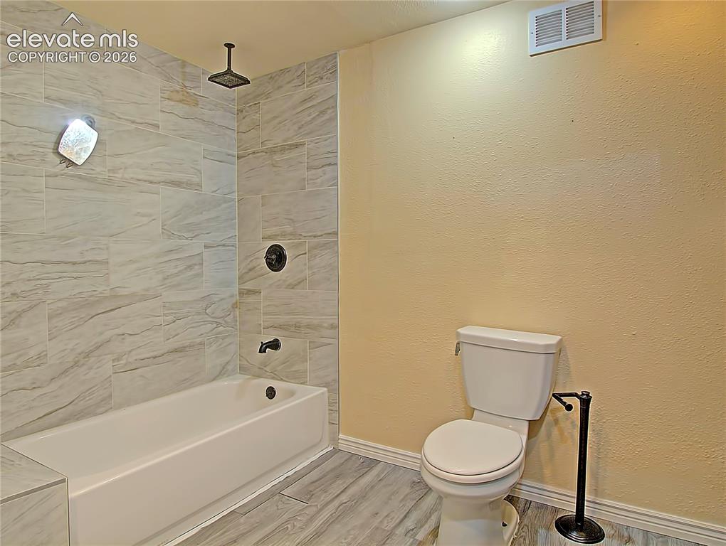 Image 21 of 28: Bathroom featuring wood-finish flooring, a white bathtub, and a toilet