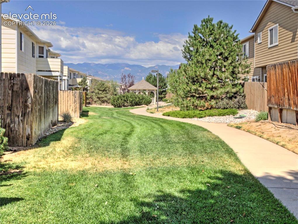 Image 27 of 28: Expansive green space featuring a paved walkway, mature evergreen trees, a