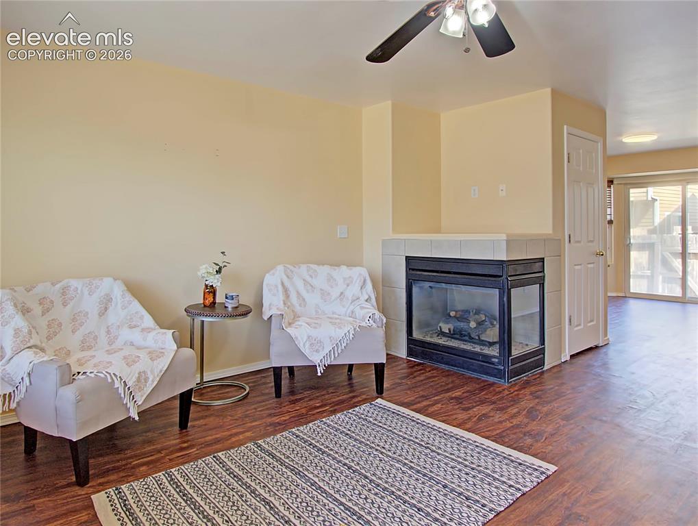 Image 4 of 28: Living area featuring wood-finish flooring, a corner fireplace with a tile