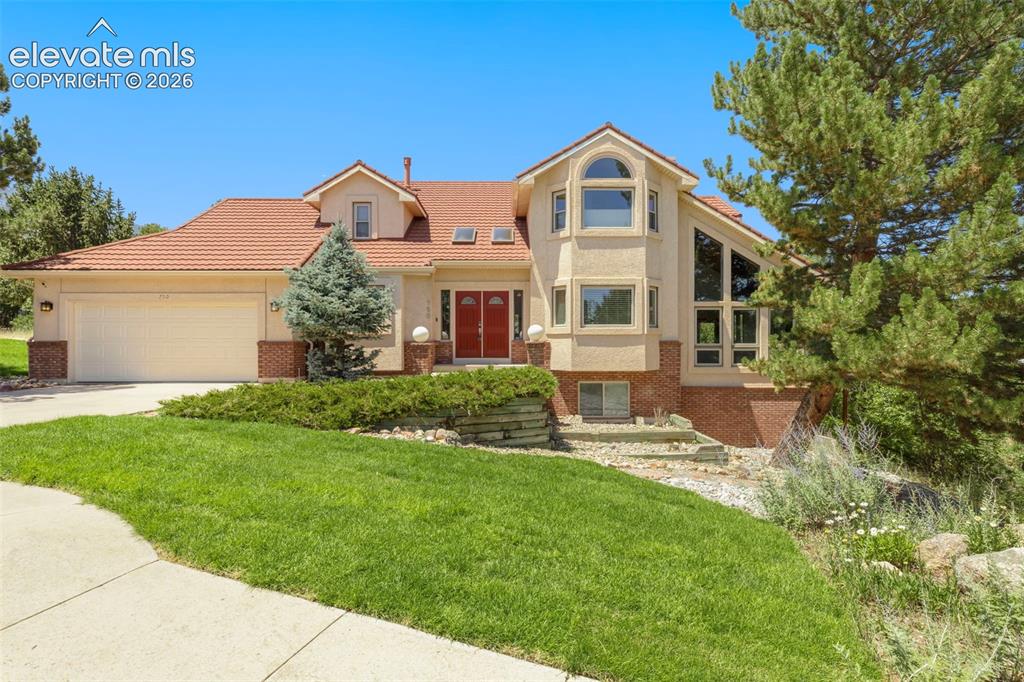 Image 3 of 46: Stucco residence featuring a red tile roof, double red entry doors, a two-c