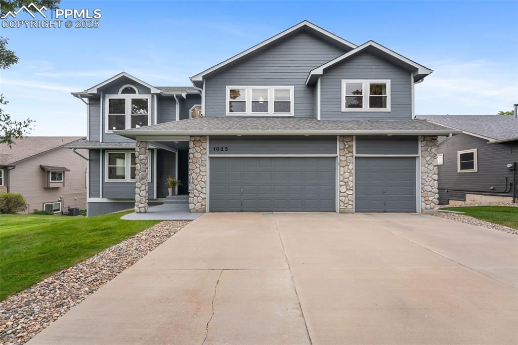 Caption: View of front of house featuring stone siding, a garage, a front yard, driveway, and roof with shing